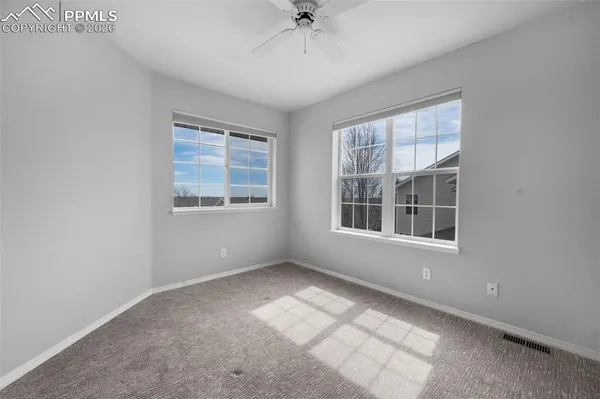 an empty room with chandelier fan and windows