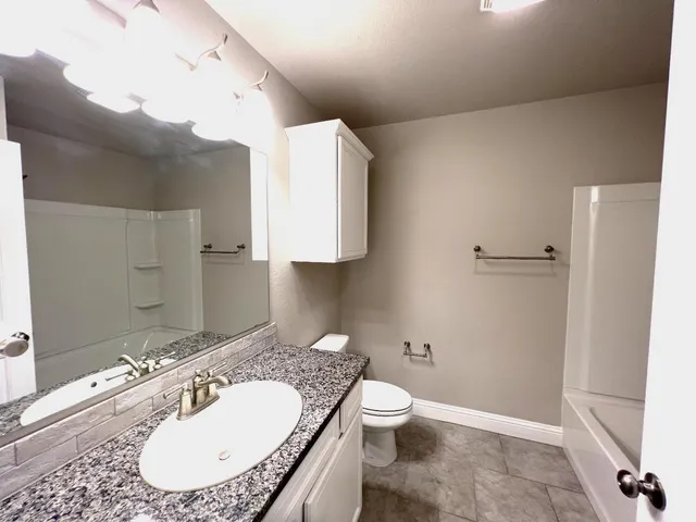 a bathroom with a granite countertop sink a toilet and a mirror
