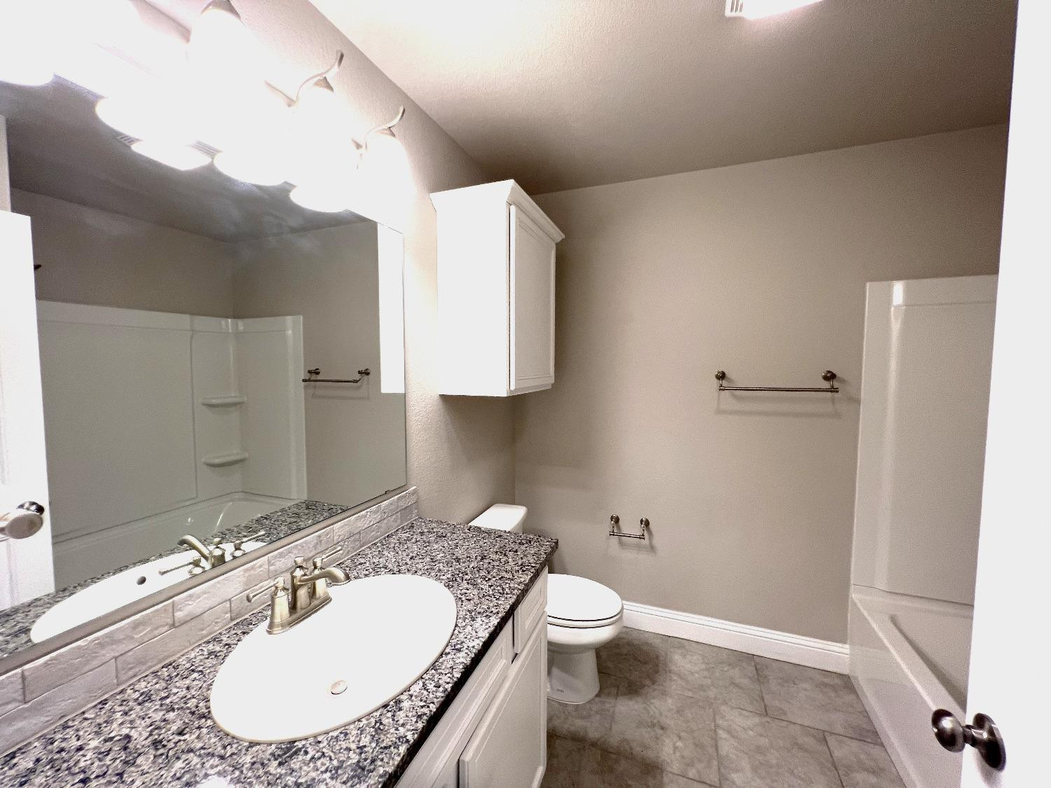 7506 100th Street Lubbock, TX 79424 - Photo 6 of 23 a bathroom with a granite countertop sink a toilet and a mirror