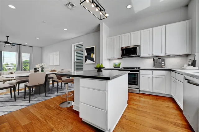 a kitchen with stainless steel appliances granite countertop a stove top oven a sink a dining table and chairs with wooden floor