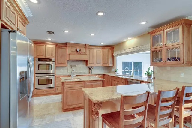 a kitchen with stainless steel appliances granite countertop a stove top oven a sink a refrigerator and chairs
