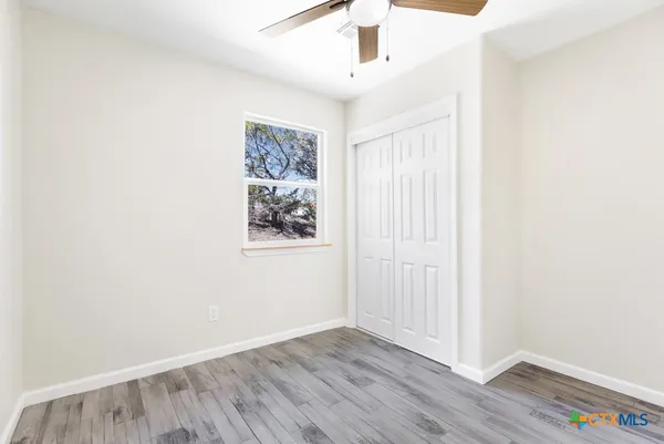 an empty room with wooden floor chandelier fan and windows