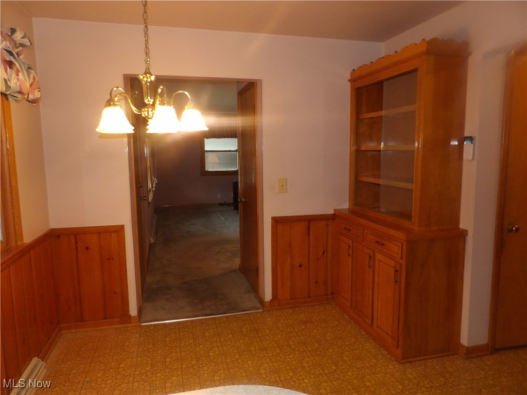 515 Hillman Road Akron, OH 44312 - Photo 8 of 17 Unfurnished dining area featuring wainscoting, wooden walls, a chandelier, and light flooring