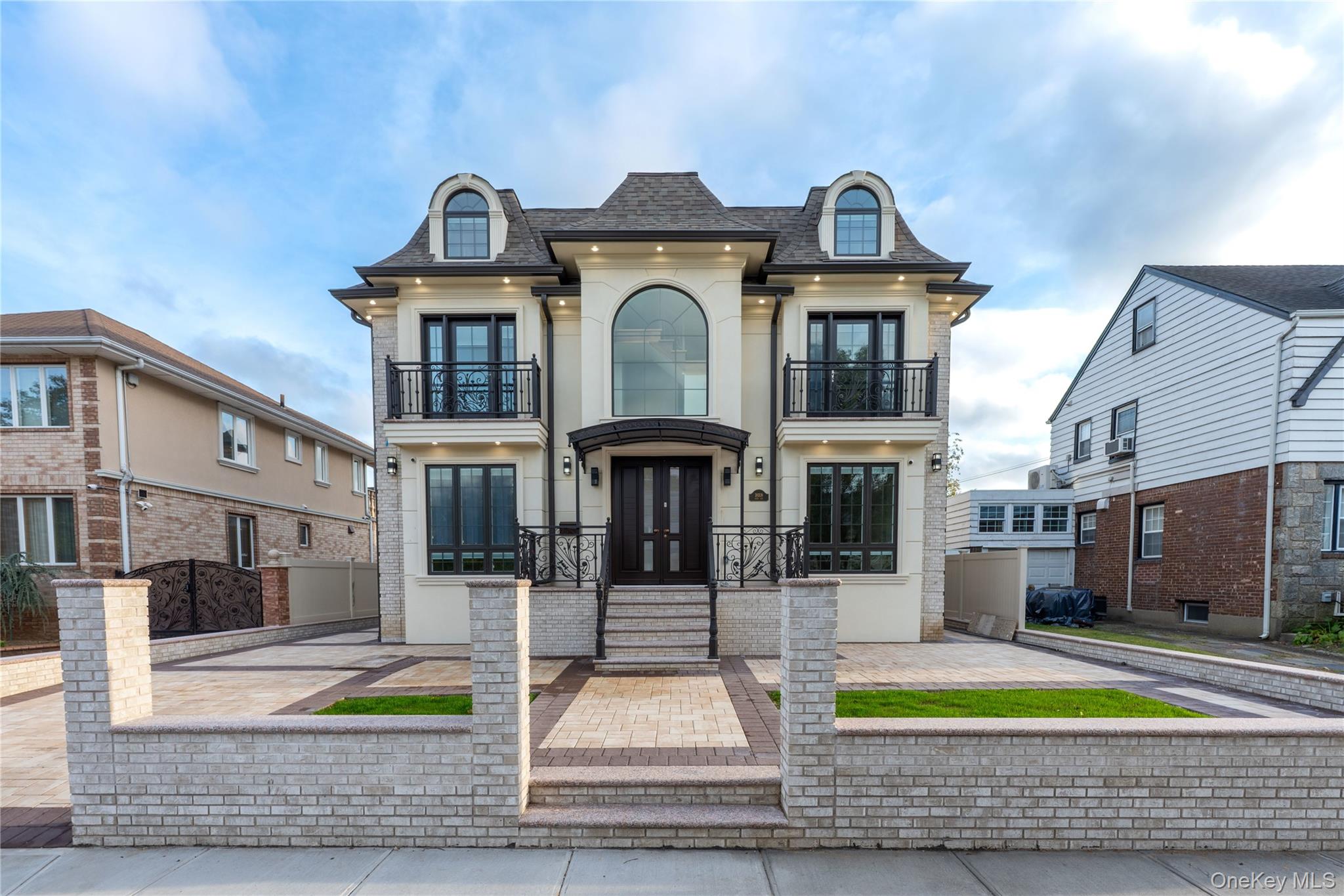 View of front of property with a balcony, roof with shingles, mansard roof, and stucco siding