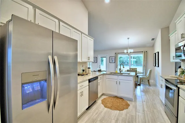 a kitchen with stainless steel appliances a refrigerator a sink dishwasher a stove and white cabinets with wooden floor
