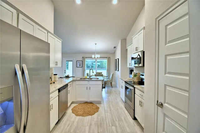 a kitchen with stainless steel appliances a refrigerator a sink a stove and white cabinets with wooden floor