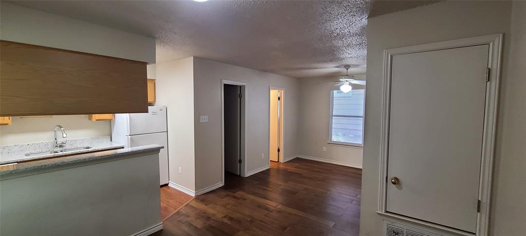 Kitchen with dark wood finished floors, a textured ceiling, freestanding refrigerator, ceiling fan, and light stone counters