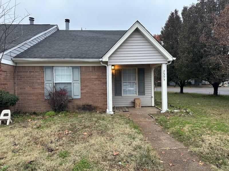 View of front facade featuring a front lawn, a shingled roof, covered porch, and brick siding
