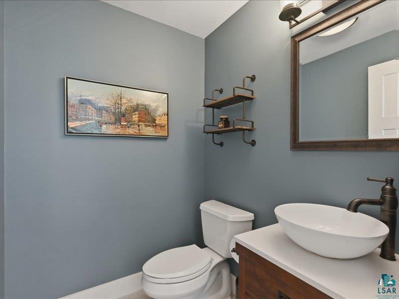 88440 Huron Street Cornucopia, WI 54827 - Photo 24 of 44 Powder room featuring a vessel sink with a dark bronze faucet, a wood-finish vanity with a light-toned countertop, and a matching framed mirror