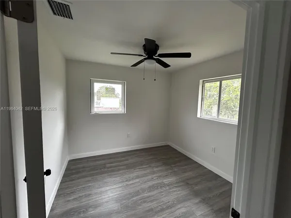 an empty room with wooden floor fan and windows