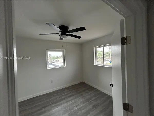 an empty room with wooden floor fan and windows