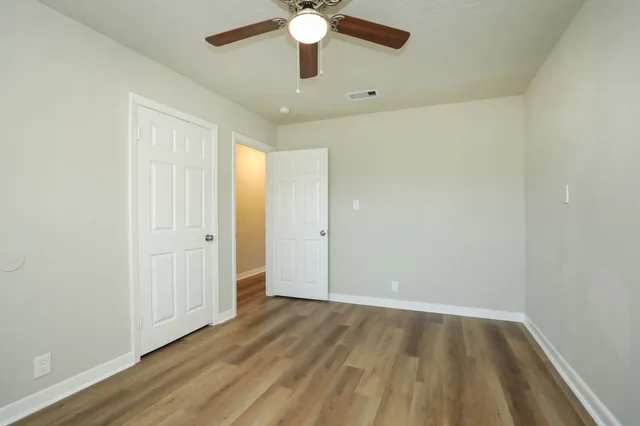an empty room with wooden floor fan and windows