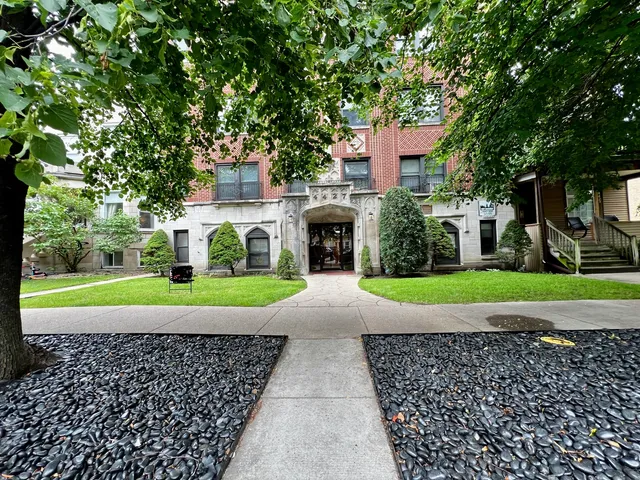 a view of a brick house with a yard and large trees