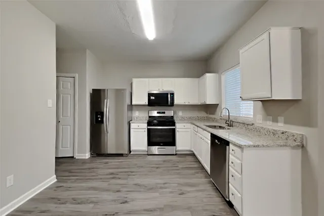 a kitchen with stainless steel appliances granite countertop a stove top oven a sink and a refrigerator with wooden floor