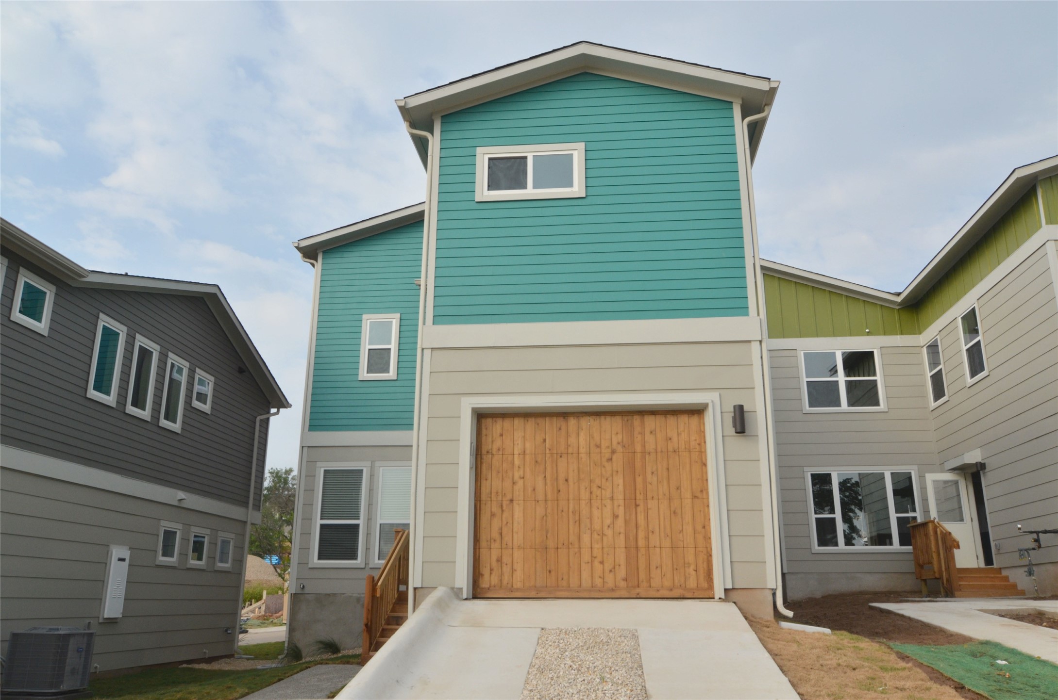 1916 Cleese Drive Austin, TX 78741 - Photo 28 of 36 A modern facade with striking teal and tan siding, showcasing a natural wood garage door.