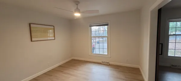 an empty room with wooden floor chandelier and windows
