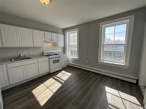 a kitchen with granite countertop a stove a sink and white cabinets with wooden floor