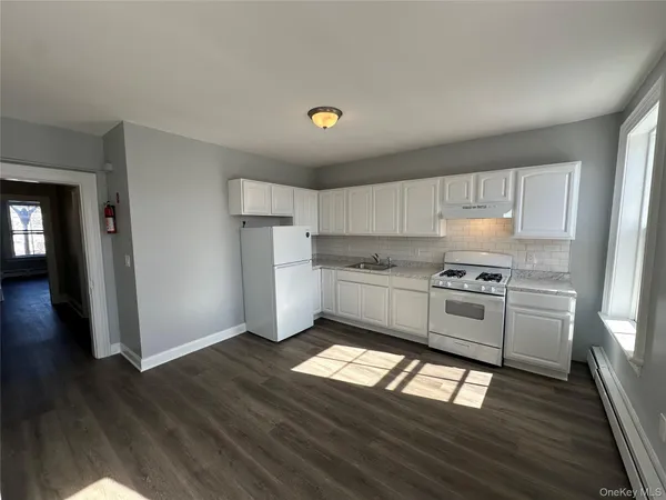 a kitchen with granite countertop a refrigerator a sink dishwasher a stove and white cabinets with wooden floor