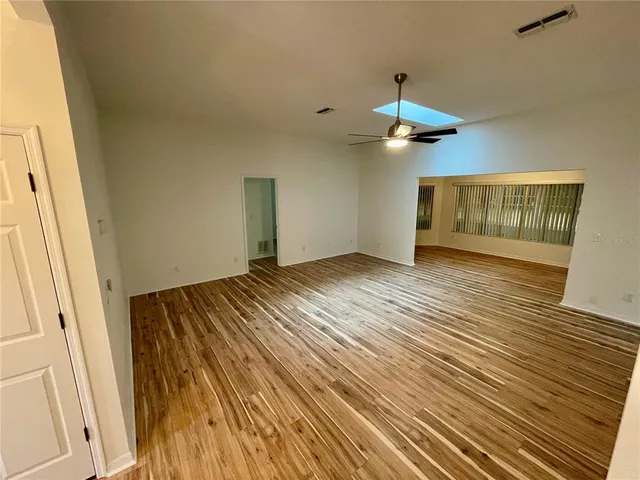a view of an empty room with wooden floor ceiling fan