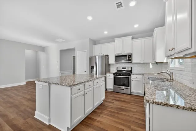 a kitchen with stainless steel appliances granite countertop a stove top oven a sink and dishwasher a refrigerator with wooden floor