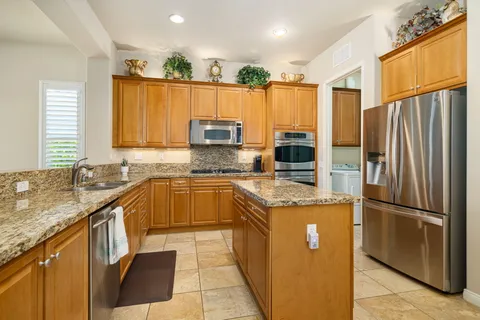 a kitchen with stainless steel appliances granite countertop a refrigerator a sink dishwasher a stove with wooden cabinets and a granite counter top