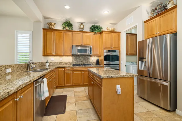 a kitchen with stainless steel appliances granite countertop a refrigerator a sink dishwasher a stove with wooden cabinets and a granite counter top
