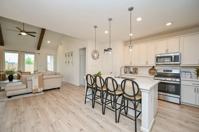 a kitchen with stainless steel appliances granite countertop a stove a refrigerator a kitchen island a dining table and chairs with wooden floor