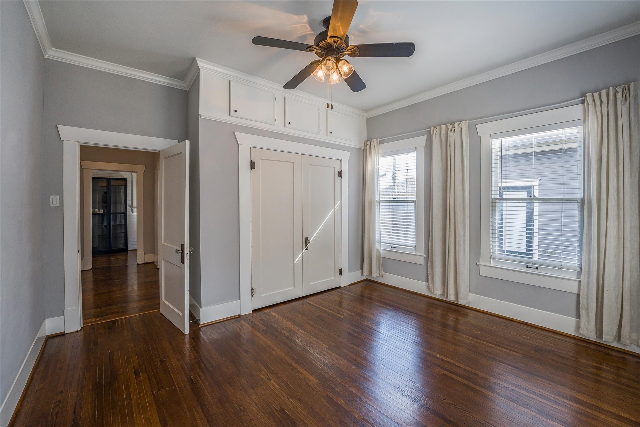 210 Tabor Street Houston, TX 77009 - Photo 8 of 18 A bright primary room with hardwood floors and neutral walls, featuring a ceiling fan, built-in storage, and two large windows with blinds and curtains, offering ample natural light.