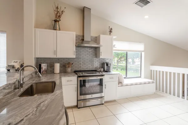 a kitchen with stainless steel appliances granite countertop a sink a stove and white cabinets with wooden floor