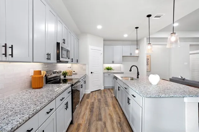 a kitchen with granite countertop kitchen island stainless steel appliances a sink a counter top space cabinets and wooden floor
