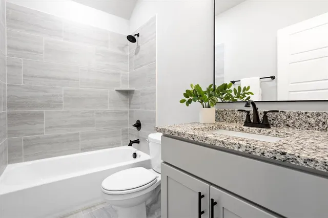a bathroom with a granite countertop sink a toilet a mirror and bathtub