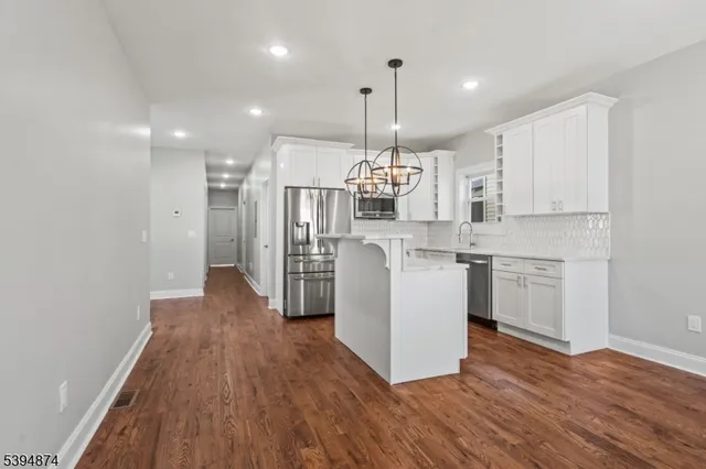 a open kitchen with stainless steel appliances granite countertop a sink a stove a refrigerator and white cabinets with wooden floor