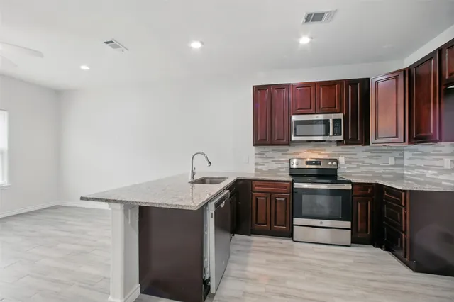 a kitchen with stainless steel appliances granite countertop a stove top oven a sink dishwasher and a microwave oven with large wooden cabinets