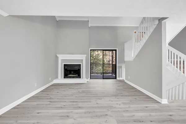 a view of an empty room with wooden floor fireplace and a window