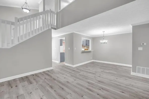 a view of an empty room with wooden floor and a kitchen