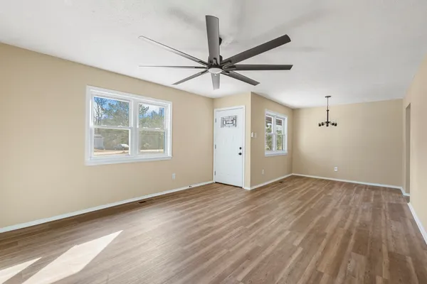 an empty room with wooden floor fan and windows