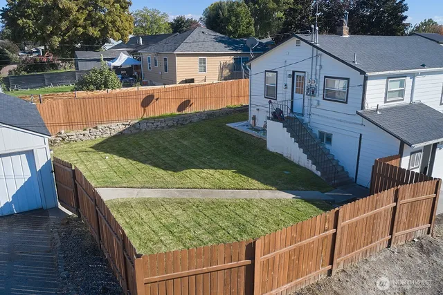 a view of a white house with a large tree and wooden fence