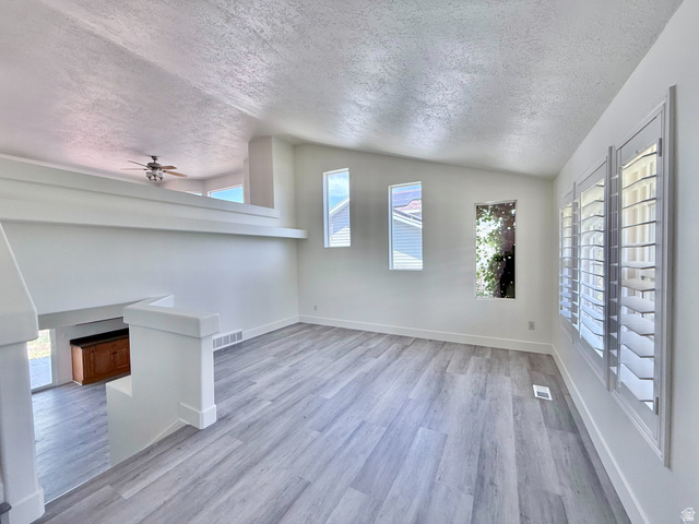 1705 80 East Tooele, UT 84074 - Photo 2 of 22 Bright living area featuring wood-finish flooring, multiple windows with plantation shutters, a vaulted ceiling, and a partial second-story overlook