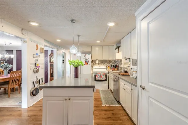 a kitchen with stainless steel appliances kitchen island granite countertop a refrigerator a oven a stove and a dining table with wooden floor