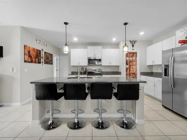 a kitchen with stainless steel appliances kitchen island granite countertop a refrigerator a stove a kitchen island and chairs with wooden floor