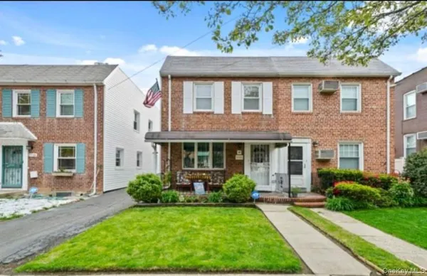 a view of a brick house with a yard plants and large tree