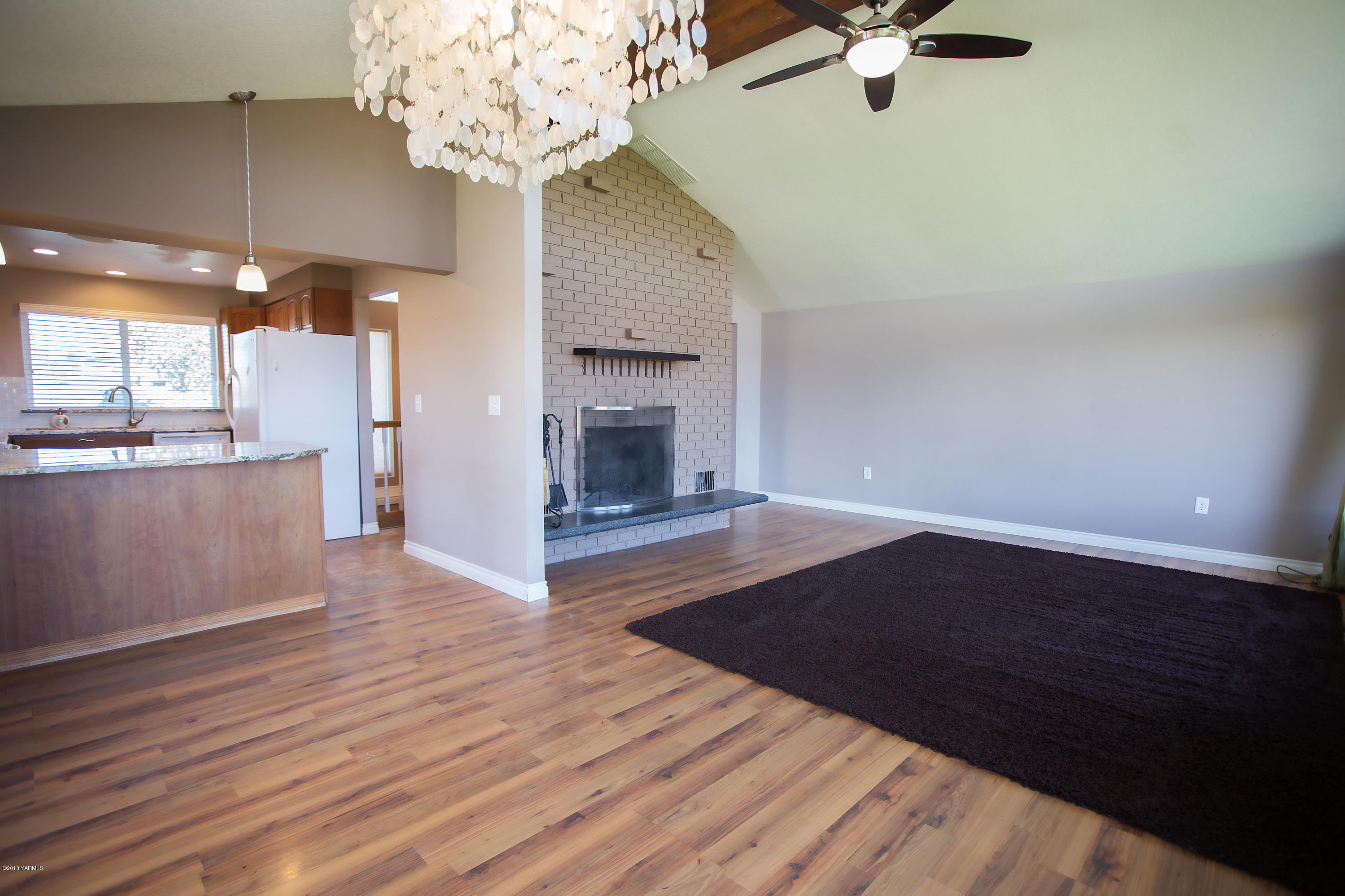 13077 Douglas Road Yakima, WA 98908 - Photo 8 of 35 an empty room with wooden floor a chandelier fan a fireplace and entryway