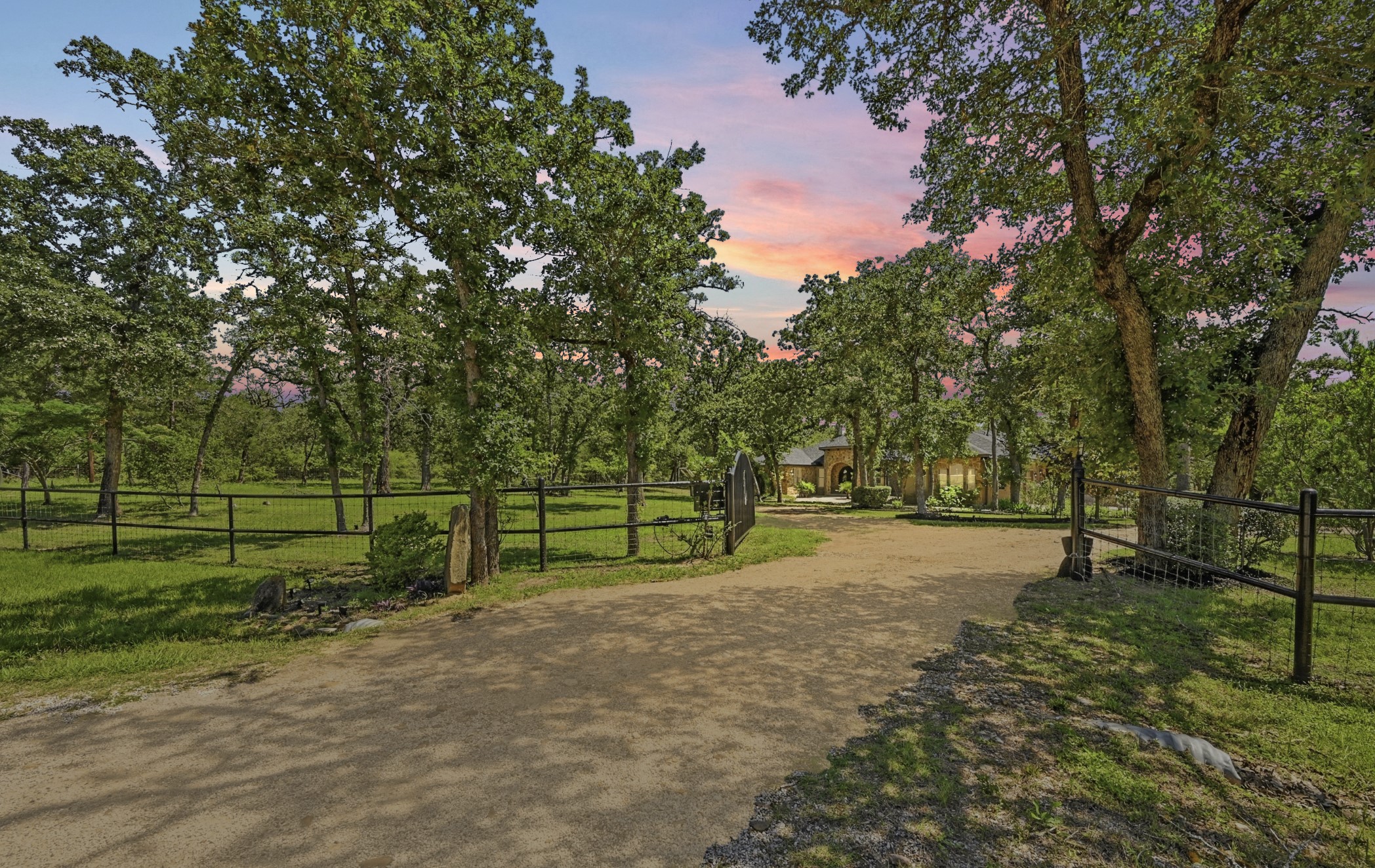 387 Corral Road Smithville, TX 78957 - Photo 9 of 40 Gated gravel driveway leading to a ranch-style residence, surrounded by mature trees and verdant lawns