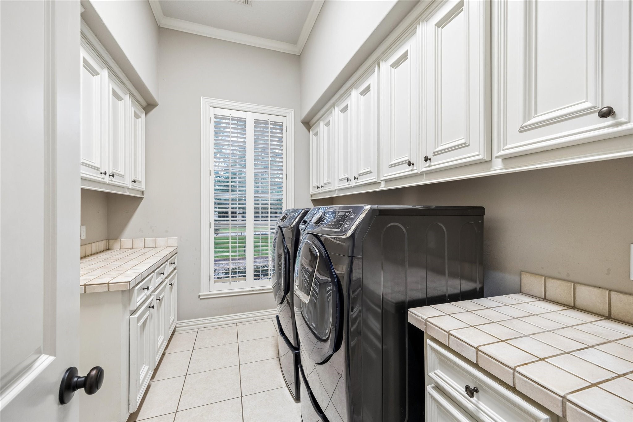 35 North Regent Oak Spring, TX 77381 - Photo 33 of 43 Designed with everyday convenience in mind, this well-appointed utility room offers abundant cabinetry, generous countertop workspace for folding and organizing, and plenty of storage to keep household essentials neatly tucked away. Natural light from the plantation-shuttered window brightens the space, creating a functional and efficient laundry area that makes daily tasks feel effortless.