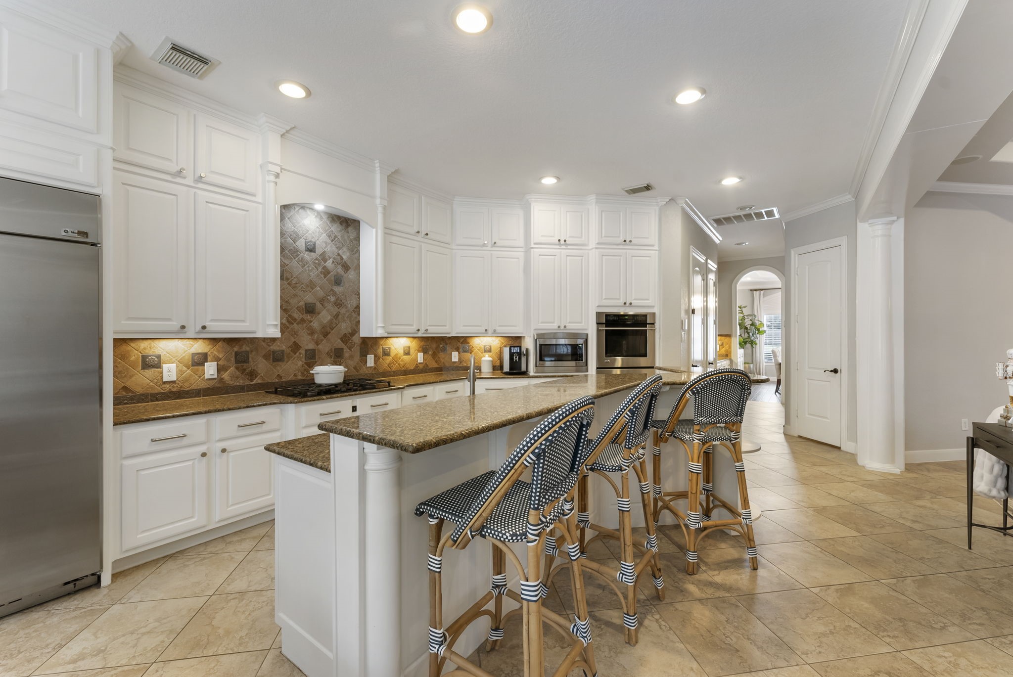 6 Lagato Place Spring, TX 77382 - Photo 14 of 42 Generous seating for casual meals and conversation. Built-in fridge, warm stone surfaces, and recessed lighting create a highly functional and welcoming space.