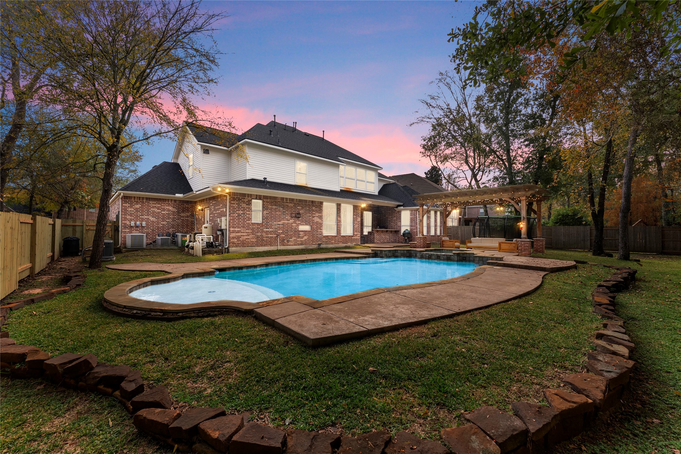 6 Lagato Place Spring, TX 77382 - Photo 33 of 42 The backyard transforms into a private retreat with a resort-style pool, expansive patio, and pergola for shaded lounging. Twilight lighting creates an inviting atmosphere ideal for evening entertaining.