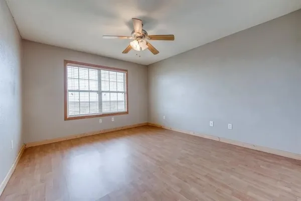 an empty room with wooden floor chandelier fan and windows