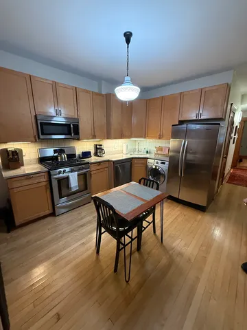 a kitchen with stainless steel appliances granite countertop a stove a refrigerator a kitchen island a sink dishwasher a dining table and chairs with wooden floor