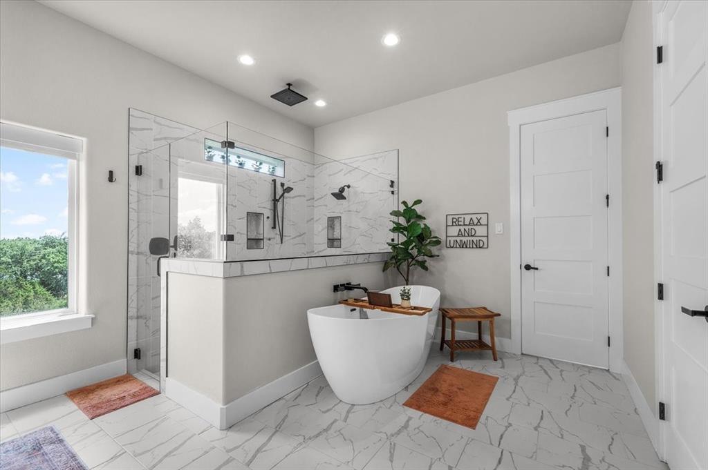 1059 Sweeney Way Weatherford, TX 76087 - Photo 13 of 37 Primary bathroom featuring a freestanding soaking tub, a spacious glass-enclosed shower with multiple showerheads, and large format marble-look tile flooring