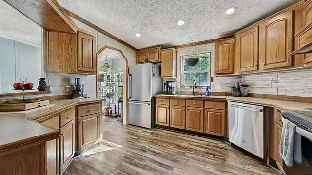 a kitchen with stainless steel appliances granite countertop a refrigerator a sink dishwasher a stove with wooden cabinets and floor